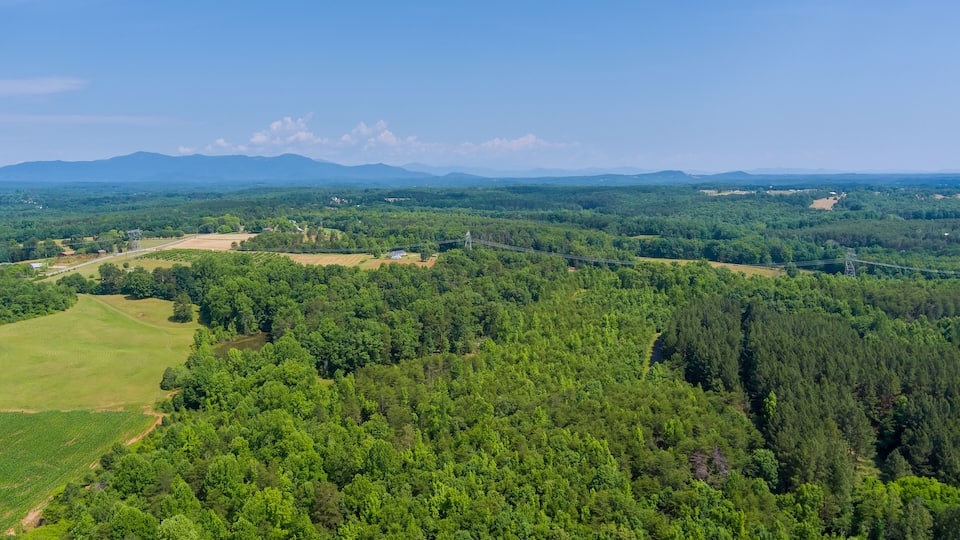 A lush green landscape with dense forests, open fields, and distant mountains under a clear sky.