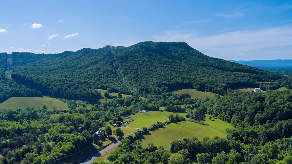 A lush green valley with rolling hills, a winding road, and a distant power line tower.