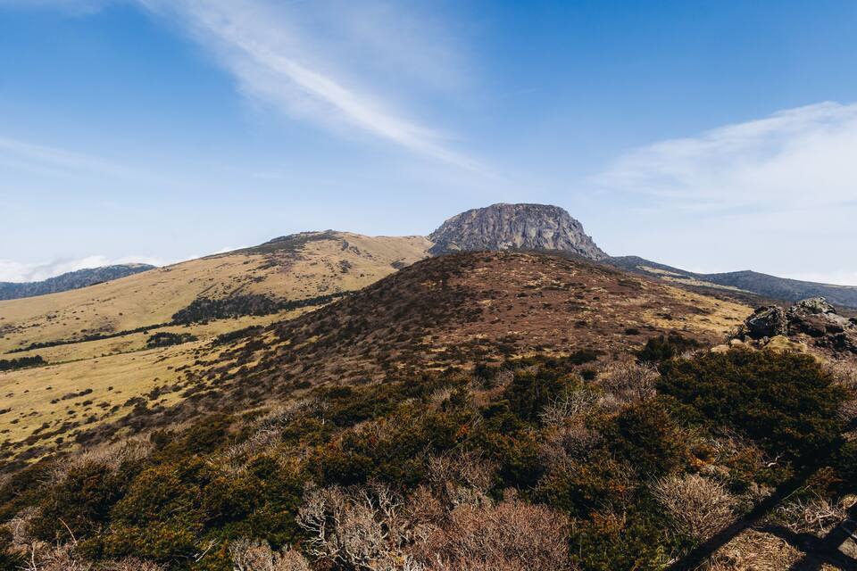 A mountainous landscape with a prominent rocky peak and sparse vegetation.