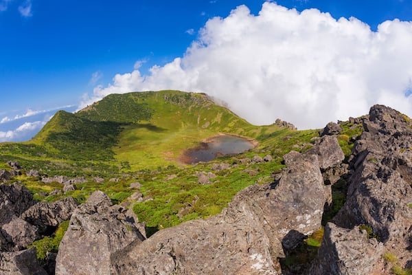 Eine Berglandschaft mit einem See, einem felsigen Vordergrund und blauem, wolkenlosem Himmel.