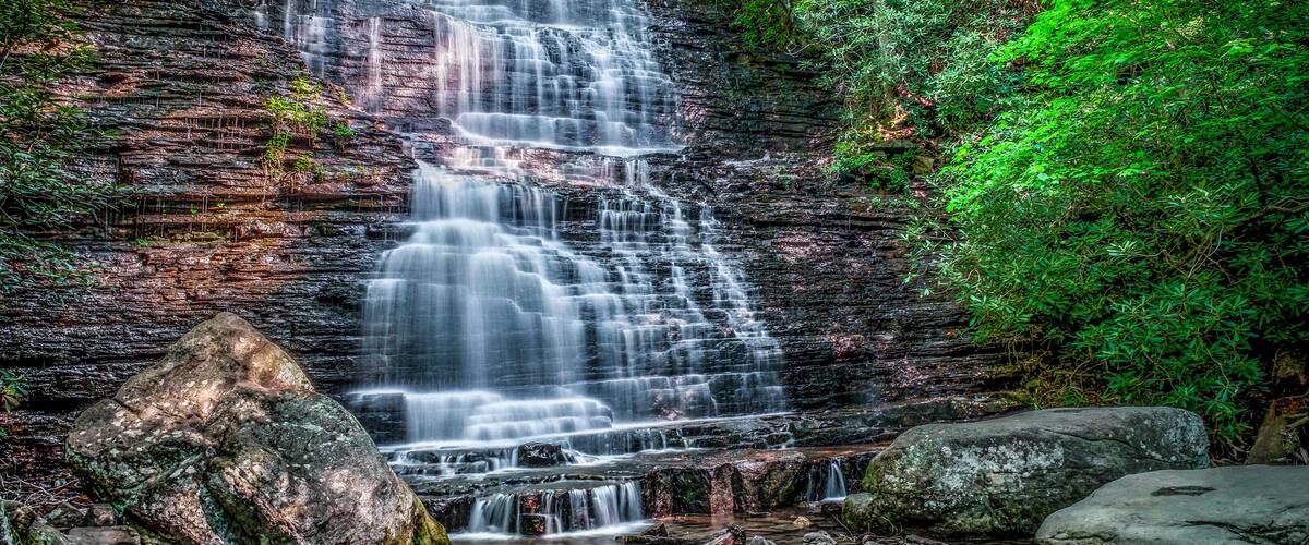 A multi-tiered waterfall surrounded by dense green foliage.