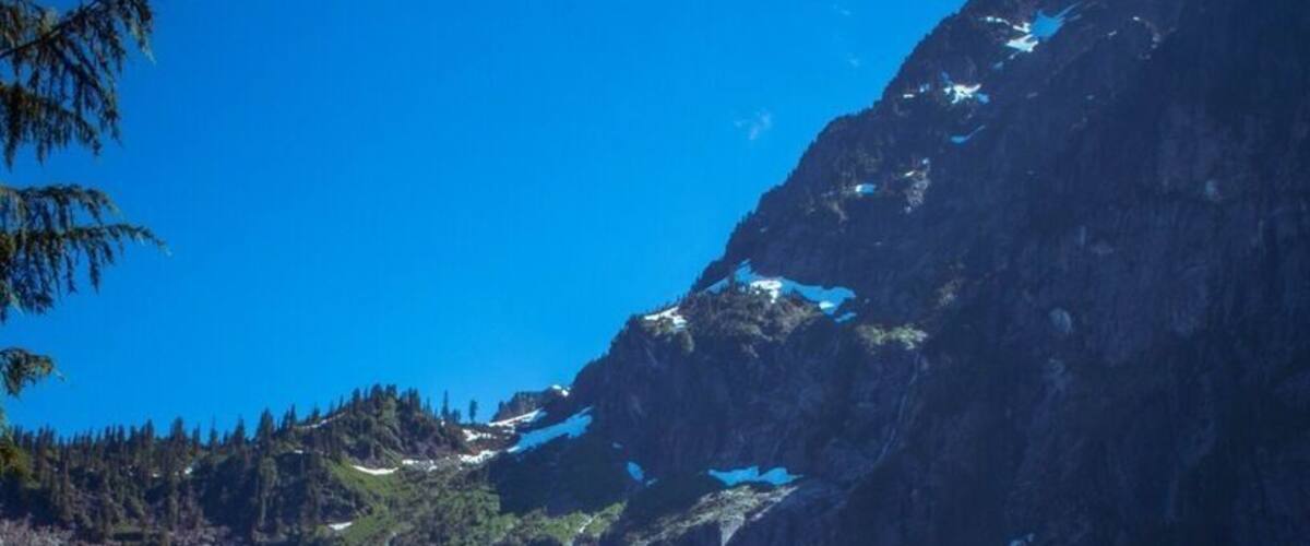 Ein Bergsee mit klarem Wasser, Schneeflecken an den Bergen und umgebender grüner Vegetation.