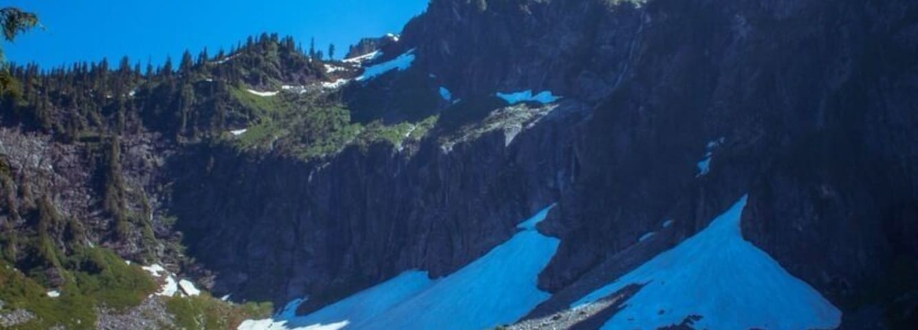 Un lago de montaña con aguas cristalinas, parches de nieve en las montañas y vegetación circundante.