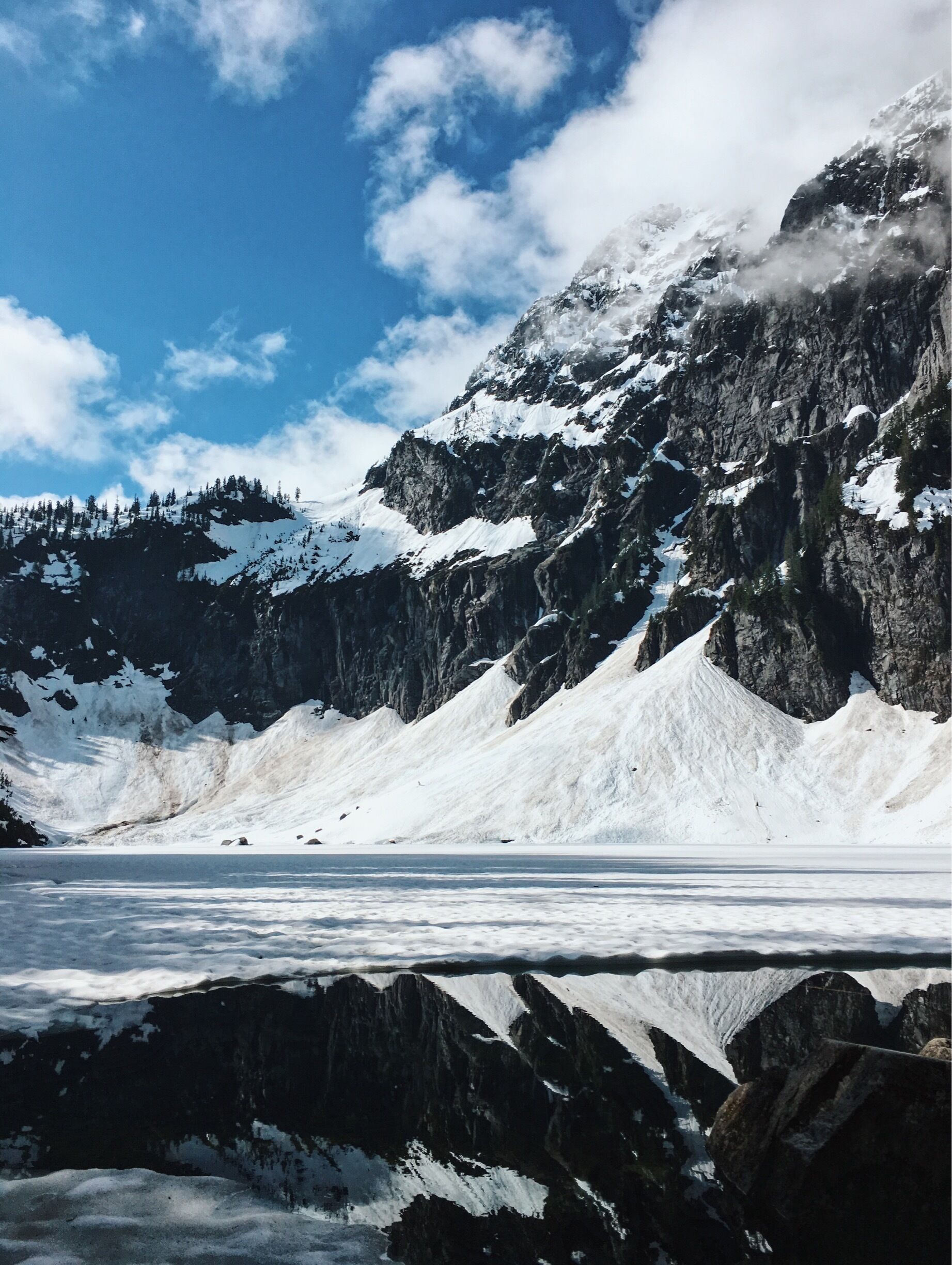 A glacier with rocky mountains and snow-covered peaks under a clear sky.