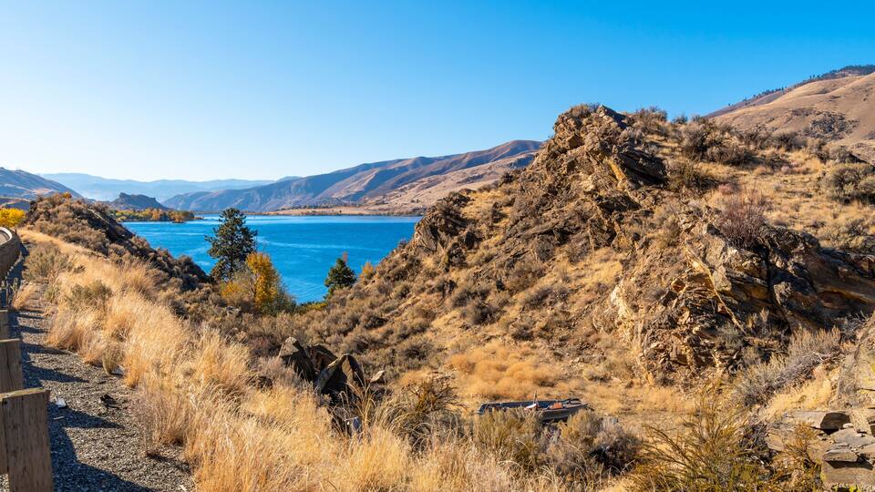 A rugged landscape with a clear blue lake surrounded by dry hills and sparse vegetation.