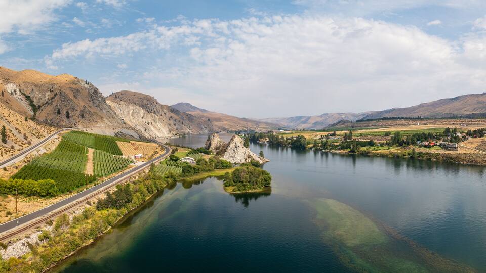 A river winding through a valley with mountains in the background, a road, and a small settlement near the water.