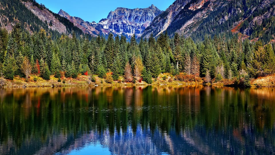 A calm lake reflecting mountains and dense forest.