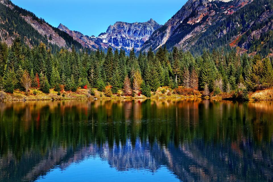 A calm lake reflecting mountains and dense forest.