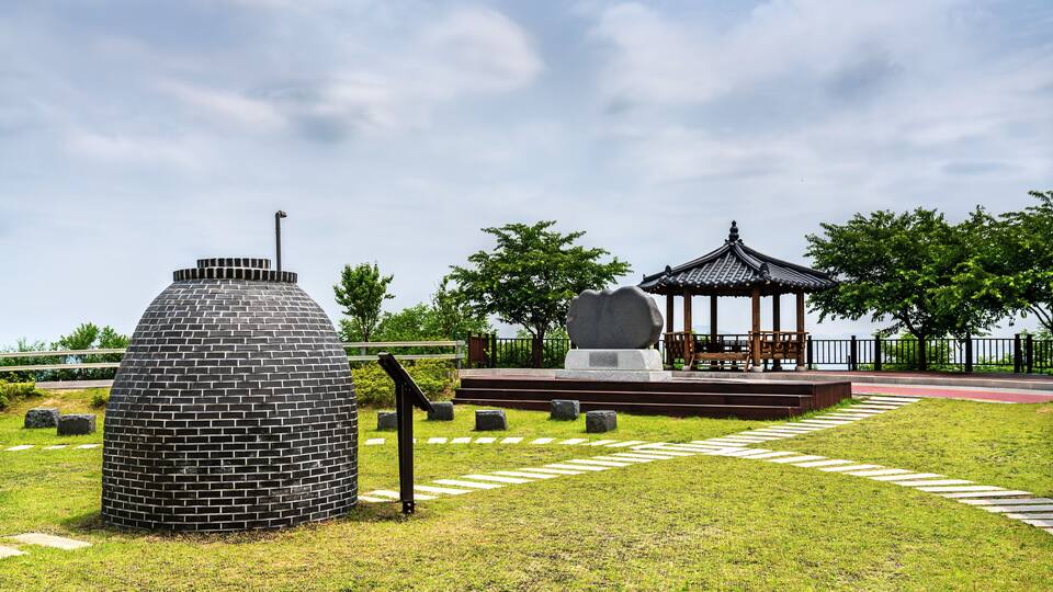 A park with a brick structure, a stone monument, and a traditional gazebo.