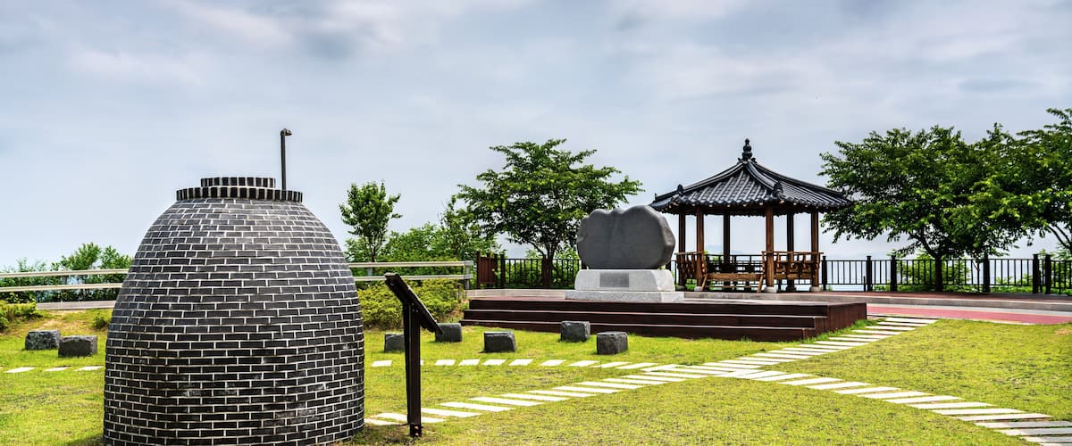 A park with a brick structure, a stone monument, and a traditional gazebo.