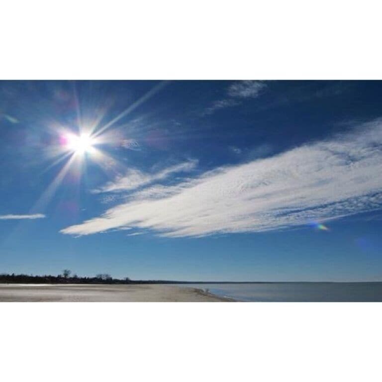 A clear sky with the sun shining and a calm sea.