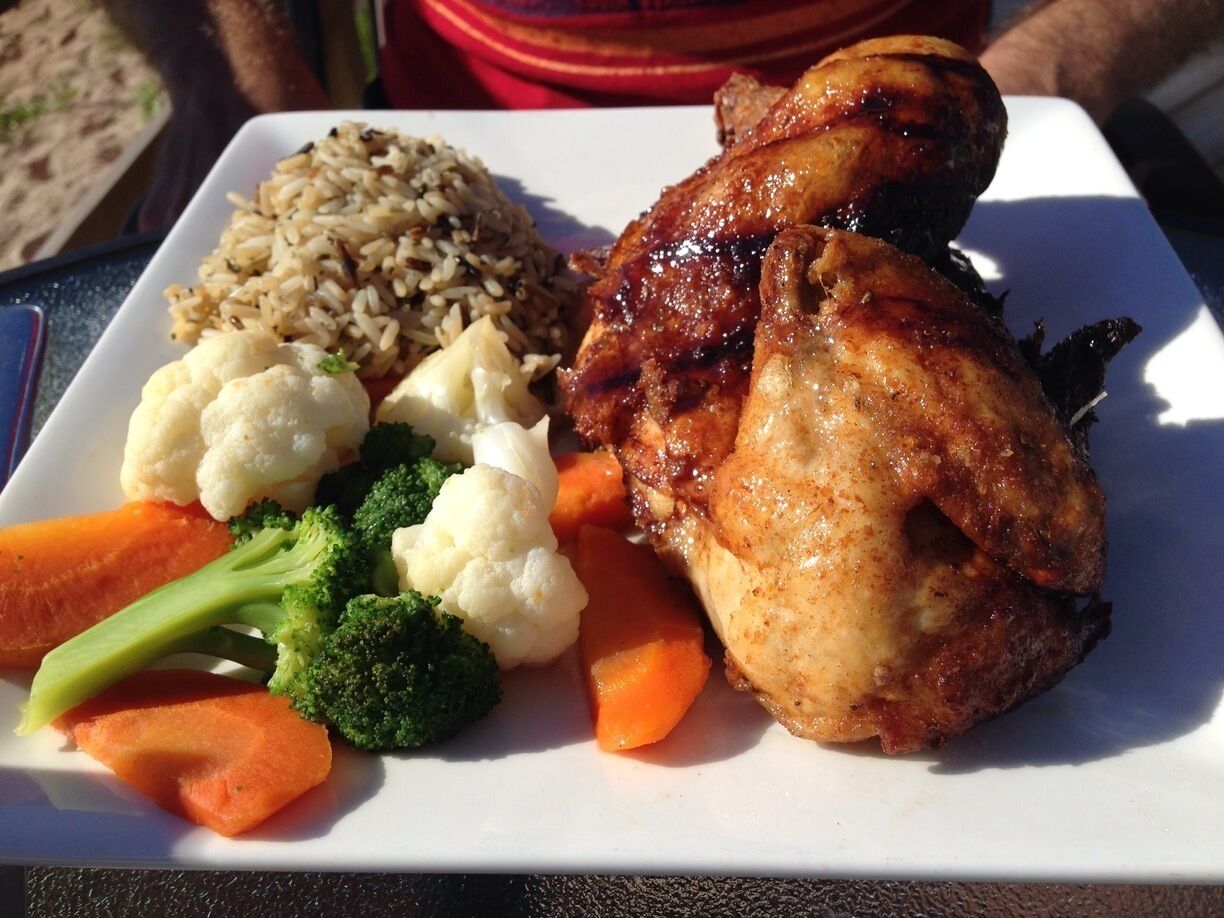 A plate of food with roasted chicken, rice, and vegetables.
