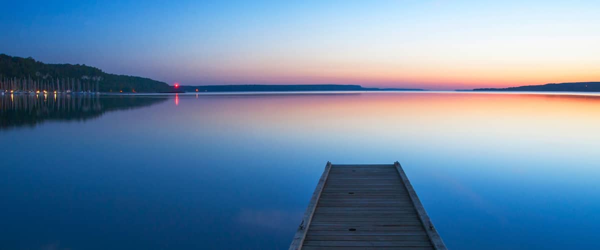A wooden dock extending into calm water at dusk with a clear horizon and distant lights.