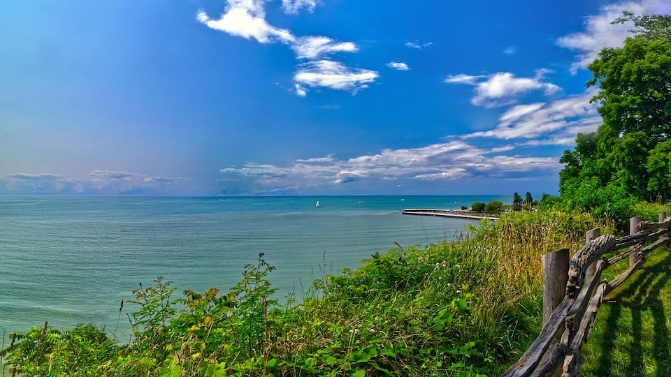 A coastal landscape with a clear sky, calm sea, and a wooden fence.