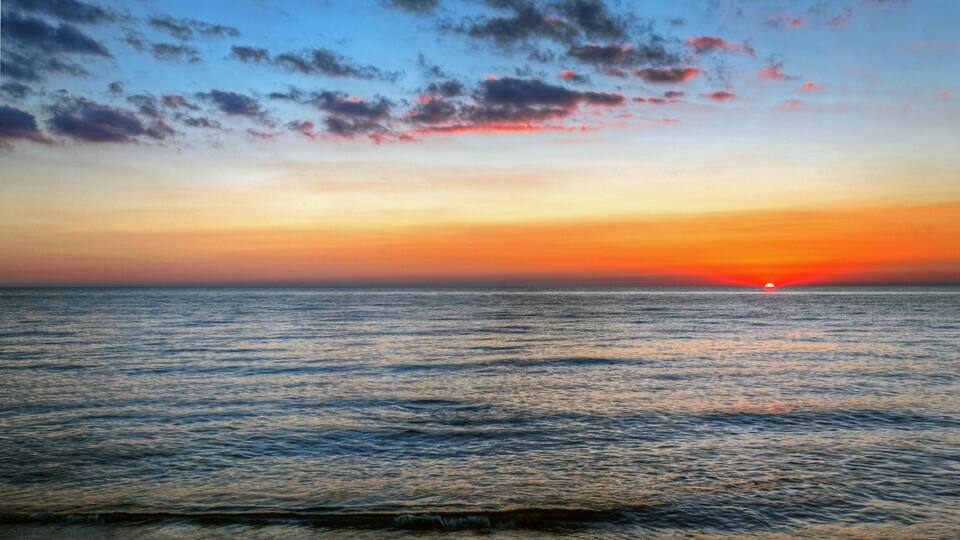 A sunset over a calm sea with a clear horizon and scattered clouds.