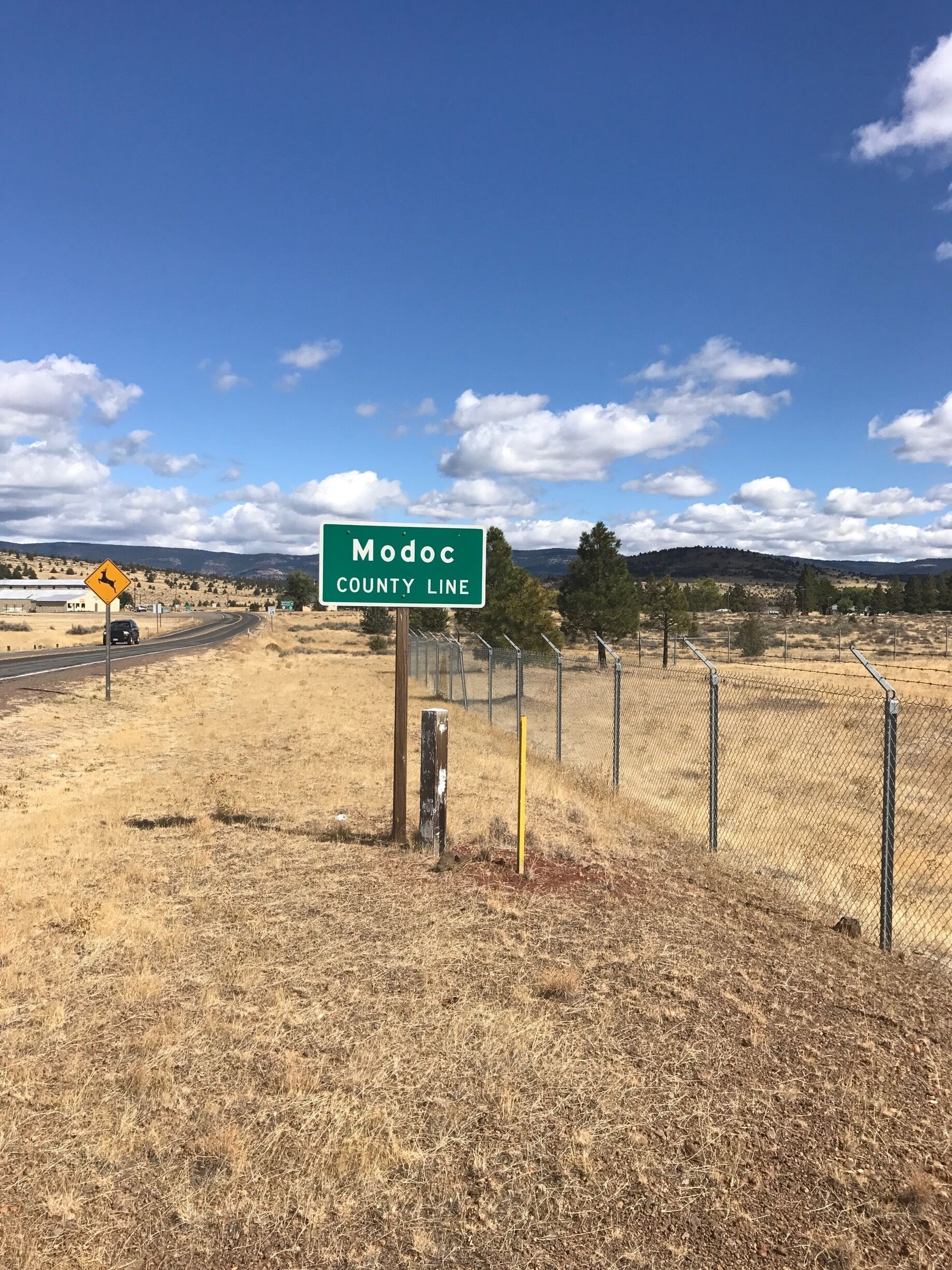 A sign for Modoc County Line with a yellow deer warning sign nearby.