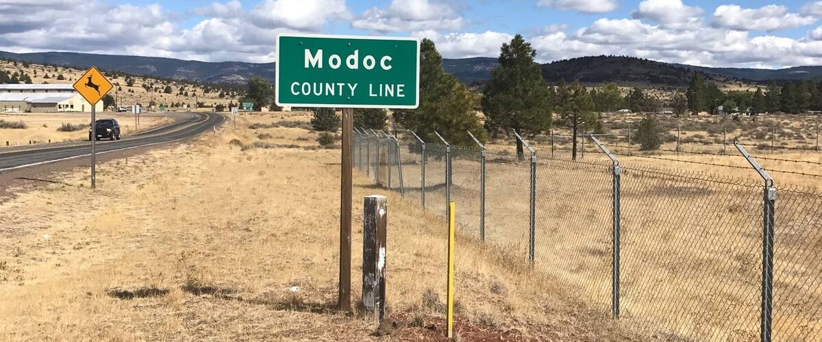 A sign for Modoc County Line with a yellow deer warning sign nearby.