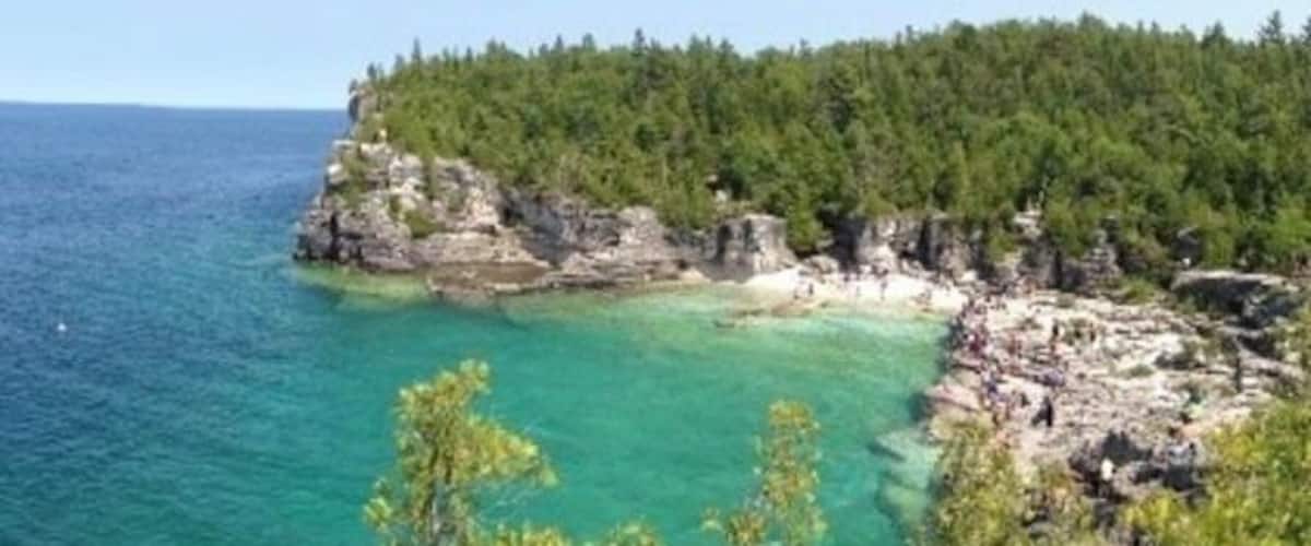 Un paisaje costero con un mar turquesa cristalino, acantilados rocosos y un bosque verde frondoso.