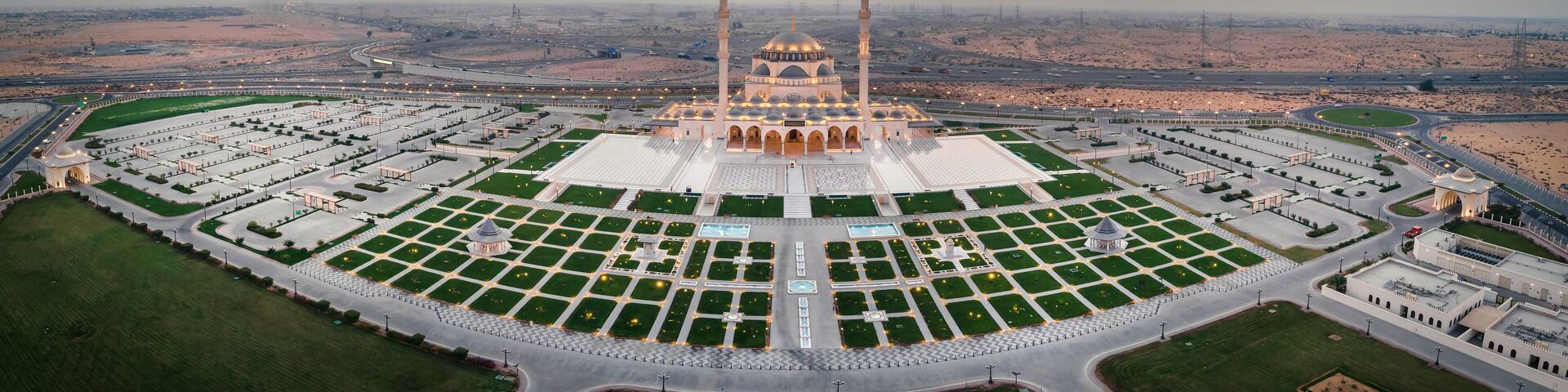 An aerial view of a mosque with a large courtyard, surrounded by roads and desert landscape.