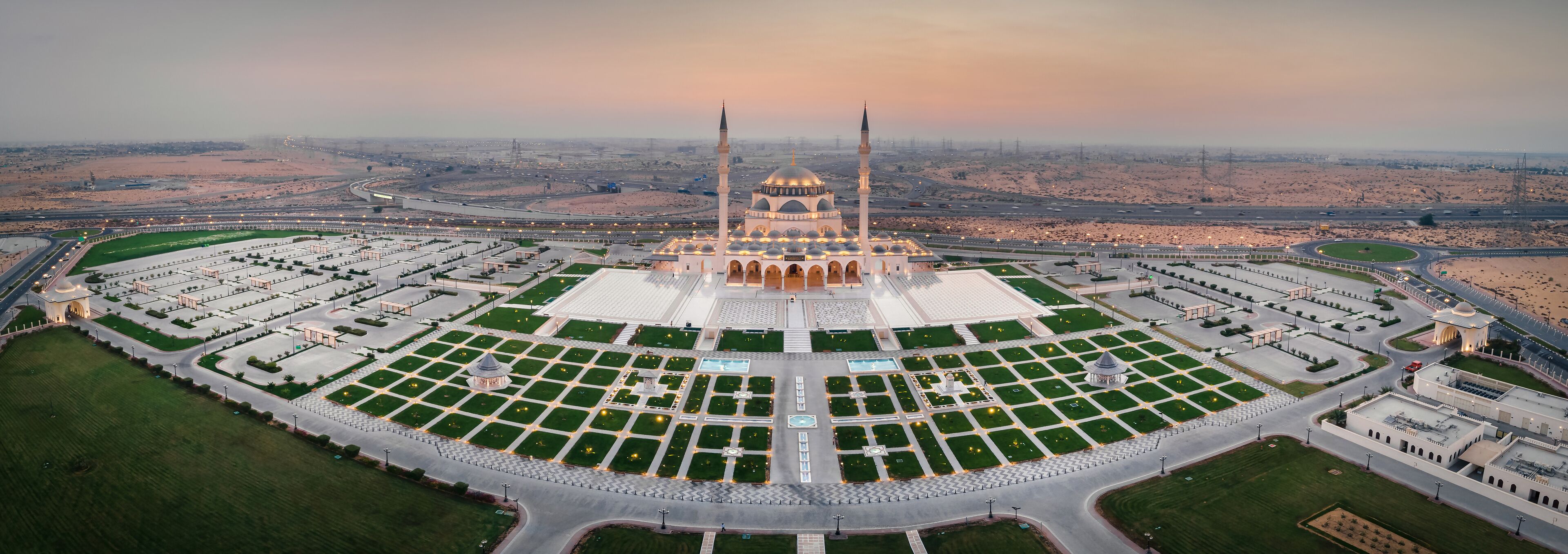 An aerial view of a mosque with a large courtyard, surrounded by roads and desert landscape.