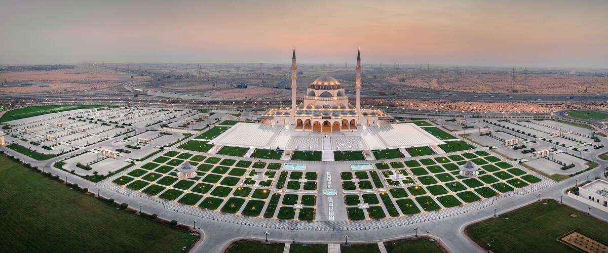 An aerial view of a mosque with a large courtyard, surrounded by roads and desert landscape.