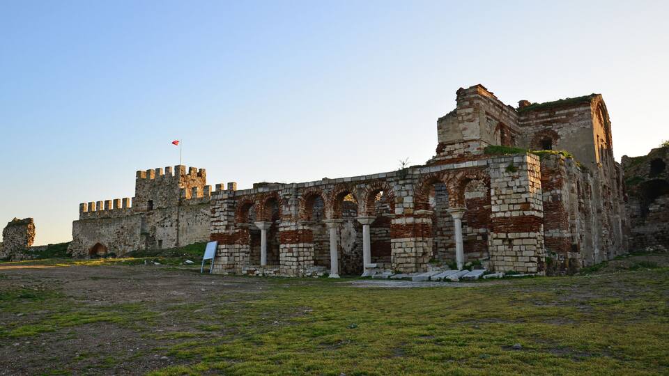 An ancient stone fortress with arched gateways and a flag atop a tower.
