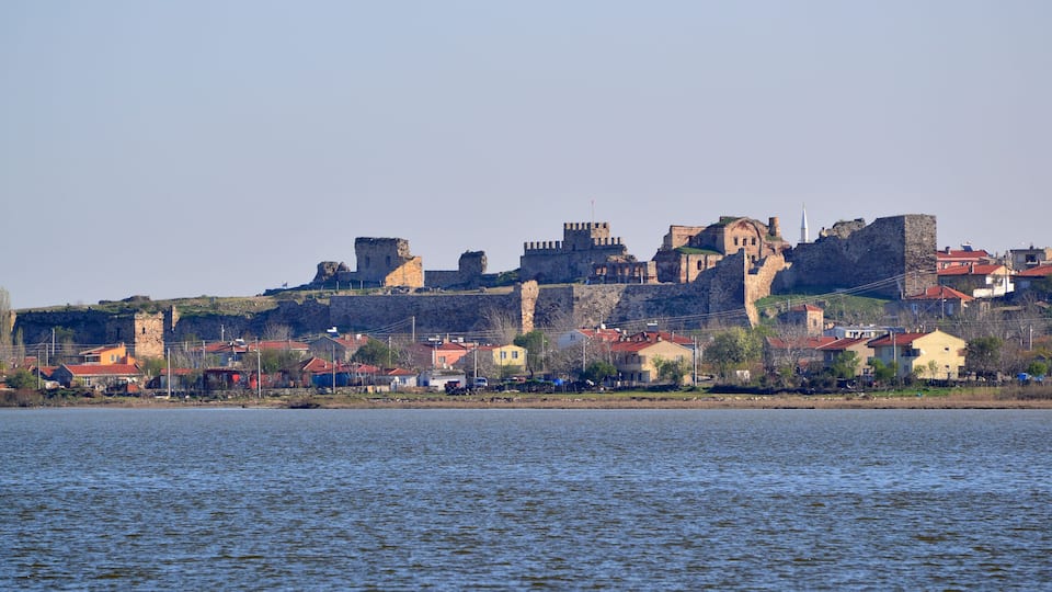 A historic castle on a hill overlooking a body of water with surrounding residential buildings.