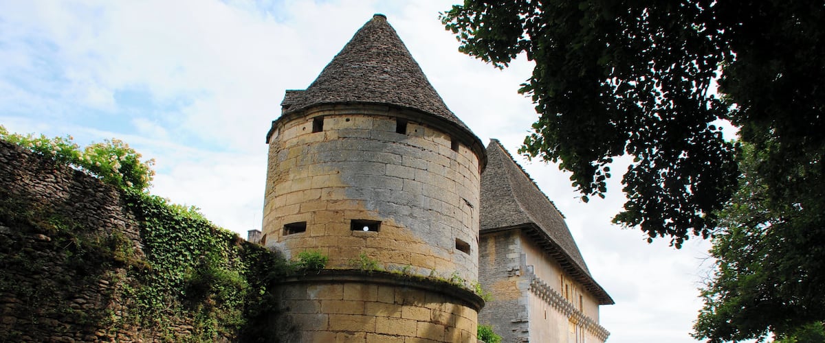 A historic stone tower with a conical roof, surrounded by ivy and a stone wall.