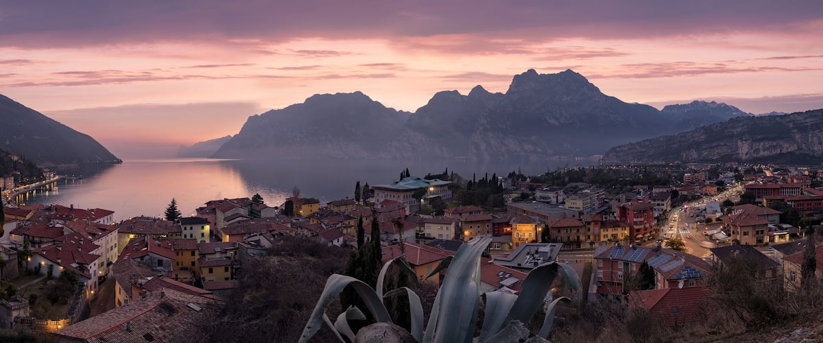 A coastal town with a mountain backdrop, a calm lake, and a mix of traditional and modern architecture.