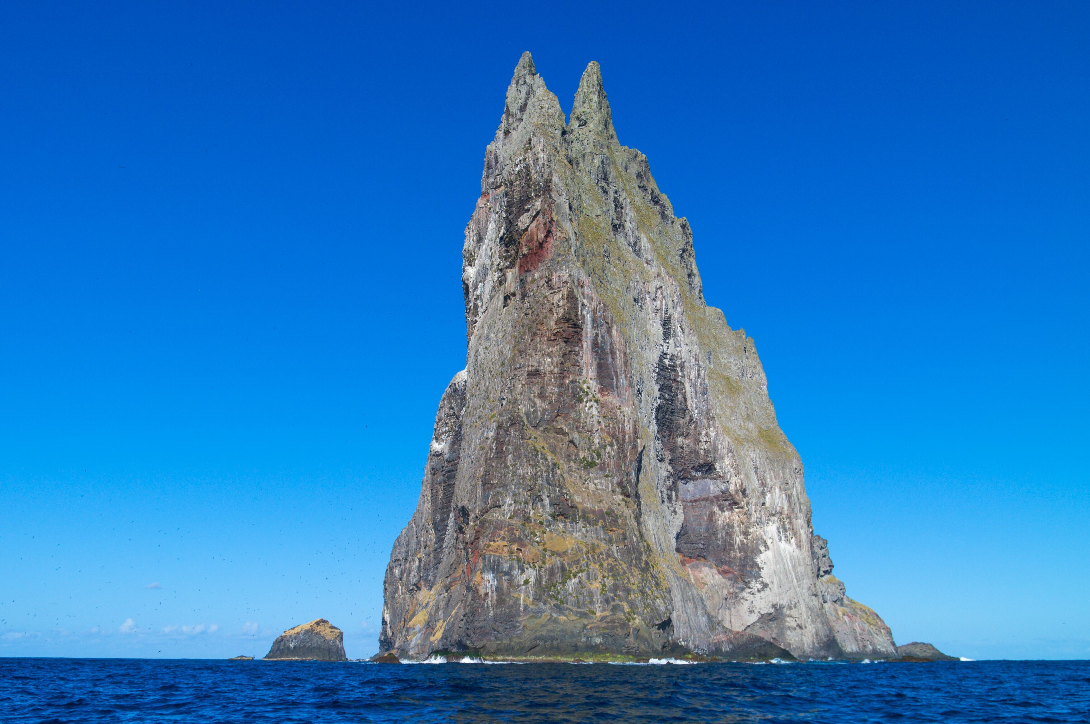 A tall, rugged cliff with a pointed peak, surrounded by deep blue ocean water.