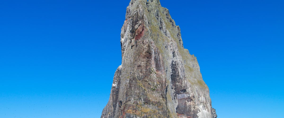 A tall, rugged cliff with a pointed peak, surrounded by deep blue ocean water.