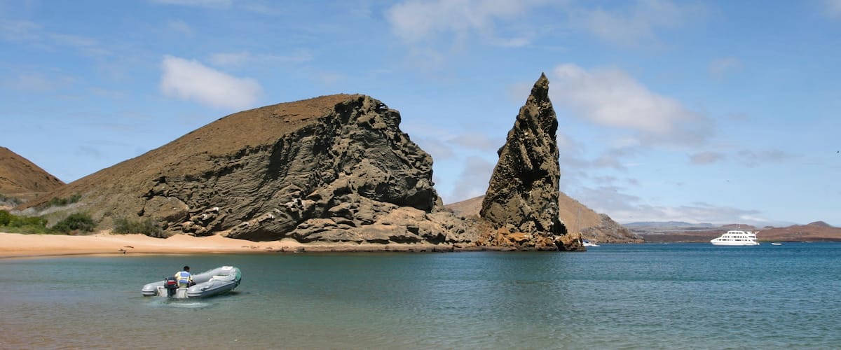 A rocky coastline with a boat in the water and a yacht in the distance.
