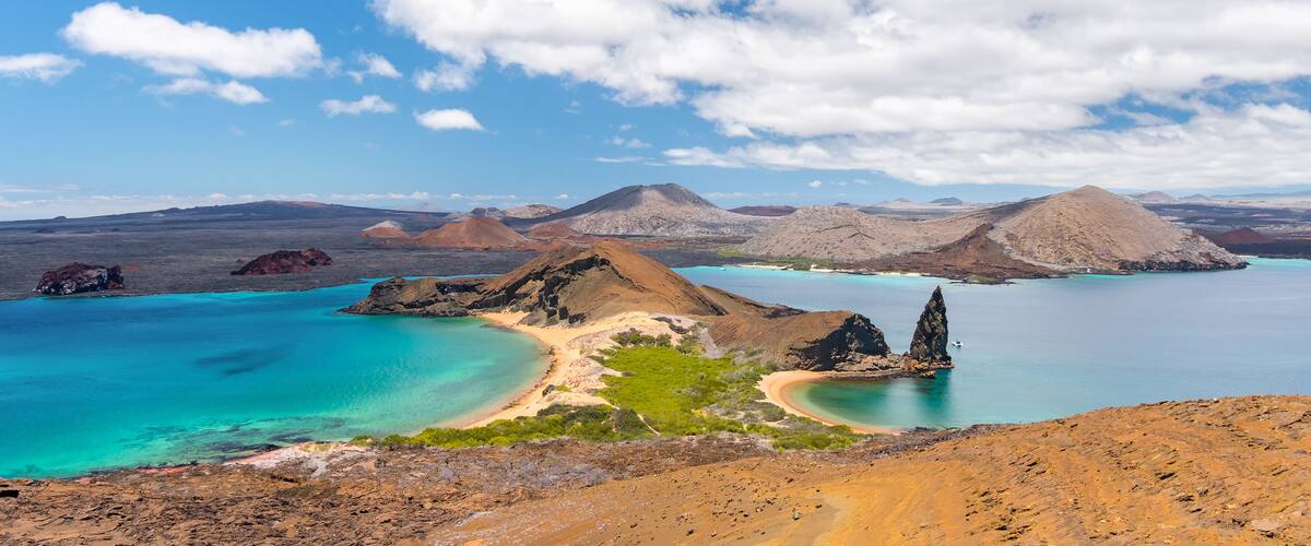 A coastal landscape with clear turquoise waters, sandy beaches, and volcanic hills.