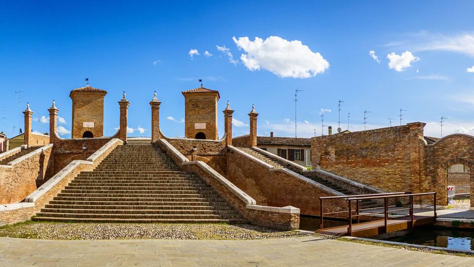 A historic staircase leading to a tower, surrounded by old brick buildings and a canal.