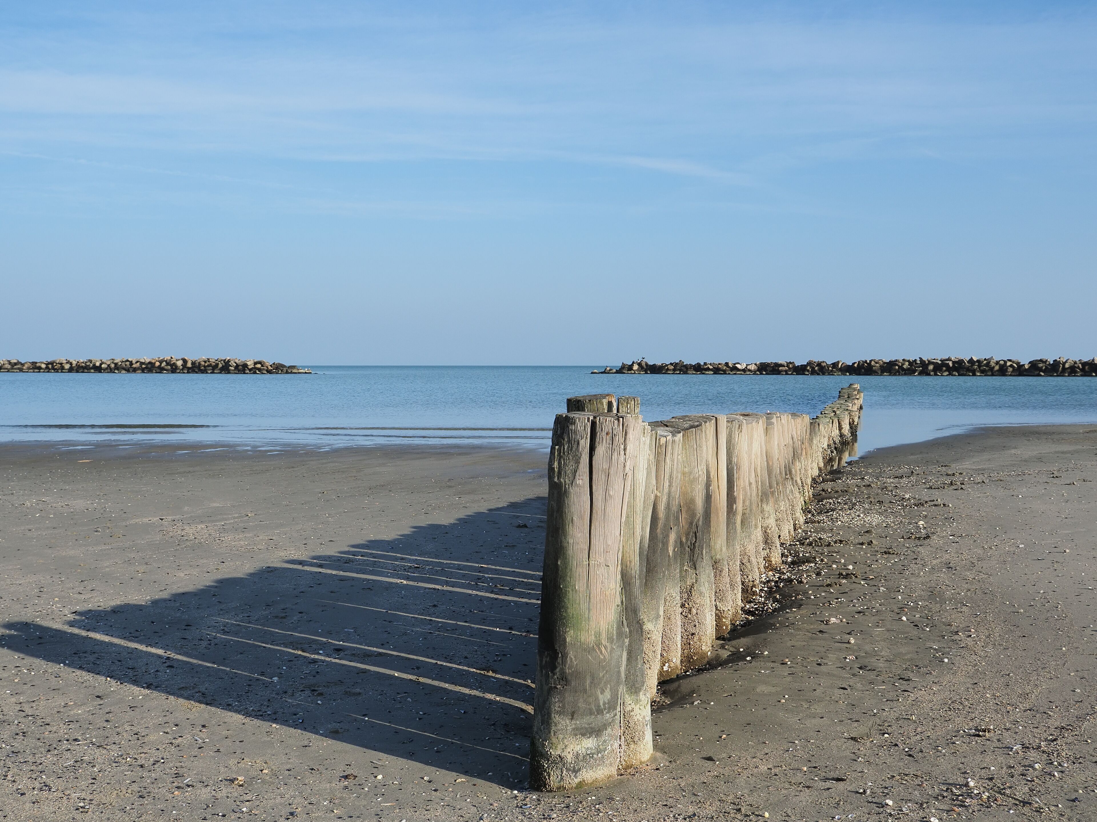 A sandy beach with wooden posts and a rocky breakwater in the background.