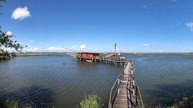 A wooden pier leading to a red building on a calm lake with clear skies.