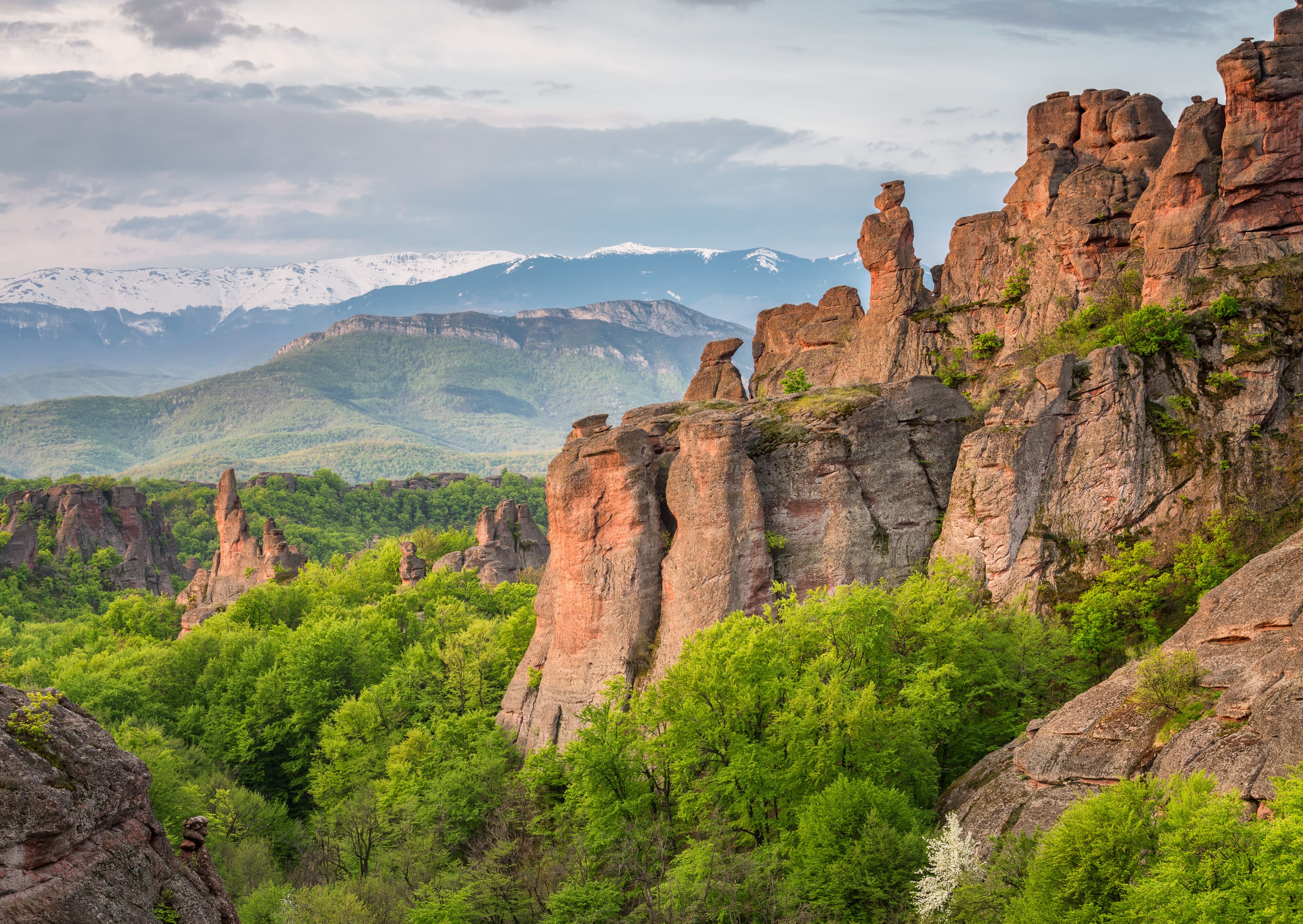 A mountainous landscape with prominent rock formations and a forested valley.