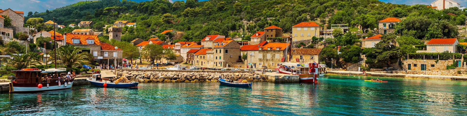 A coastal town with clear turquoise waters, boats, and buildings with red-tiled roofs.