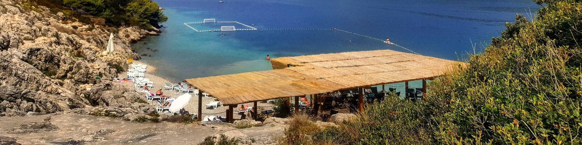 A coastal landscape with a clear blue sea, rocky shore, and a wooden structure overlooking the water.