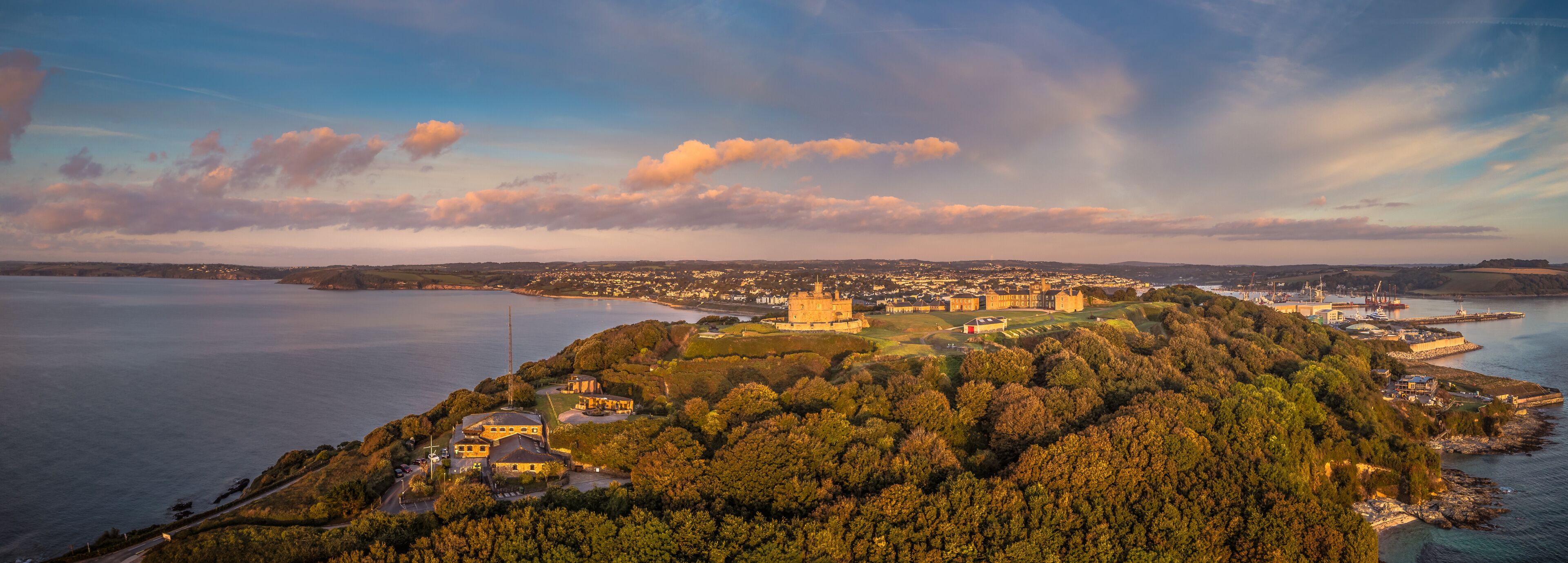 A coastal town with a prominent castle on a hill, surrounded by dense forests and a large body of water.