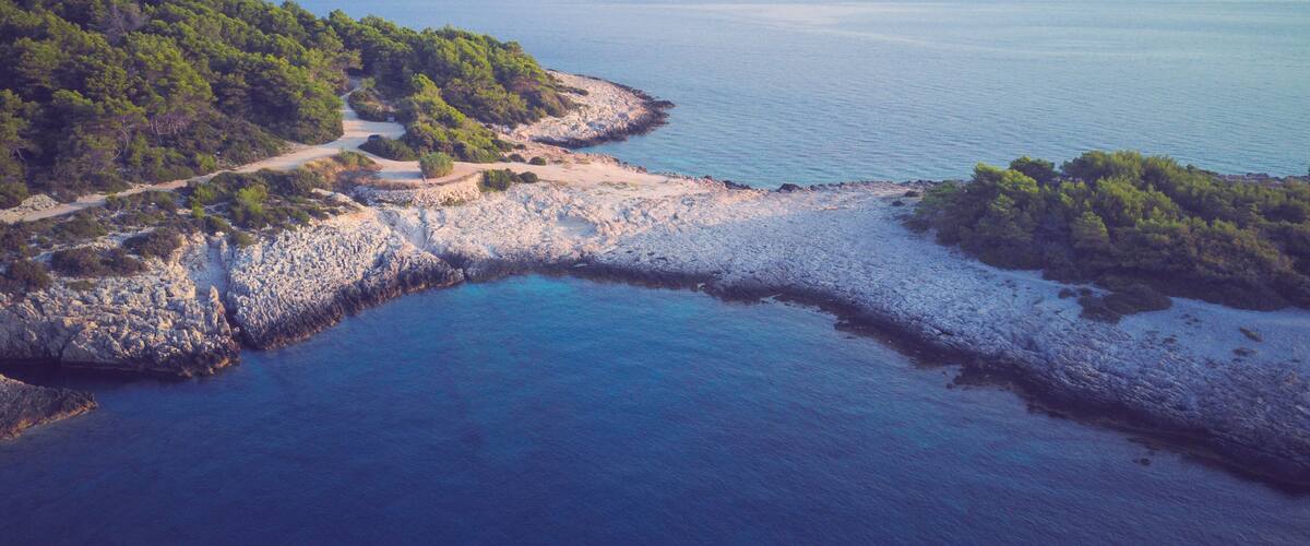 A coastal landscape with rocky shores, a clear blue sea, and distant mountains.