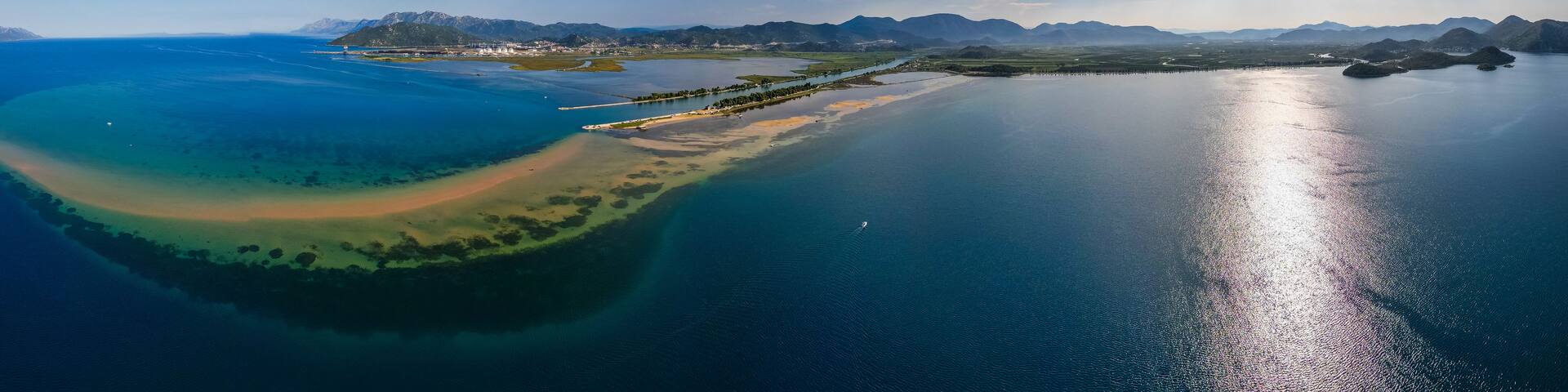 An aerial view of a coastal landscape with a clear sky, a large body of water, and a distant mountain range.