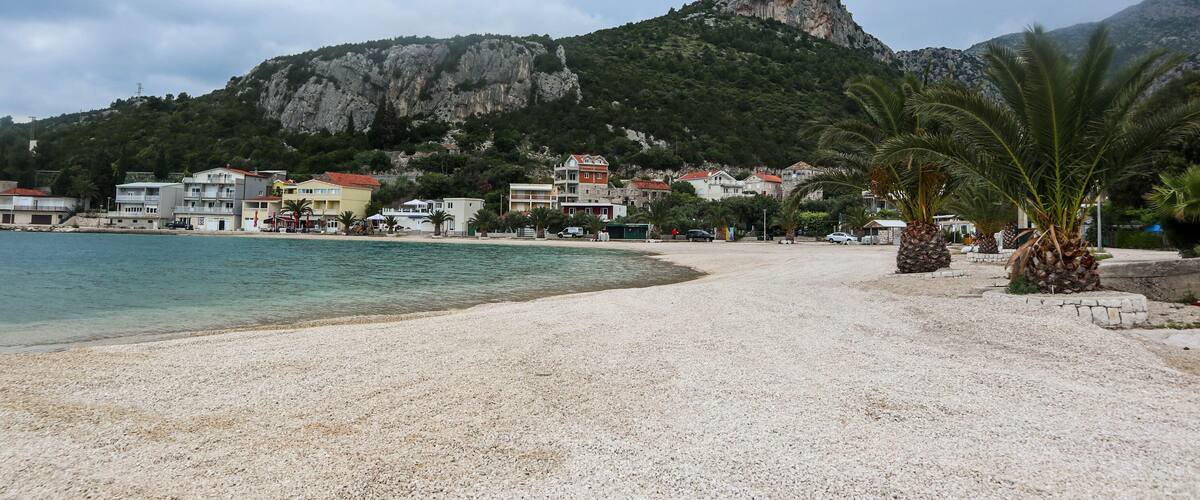 A pebble beach with buildings and a mountain in the background.