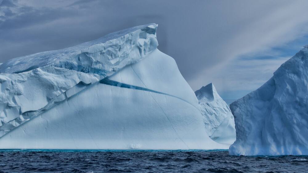 A large iceberg in the ocean with a cloudy sky.