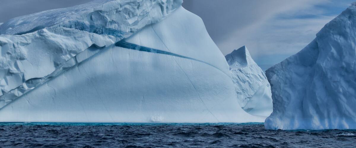 A large iceberg in the ocean with a cloudy sky.