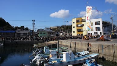 Un port où des bateaux sont amarrés, une foule de personnes et un bâtiment orné d’une bannière aux couleurs vives.