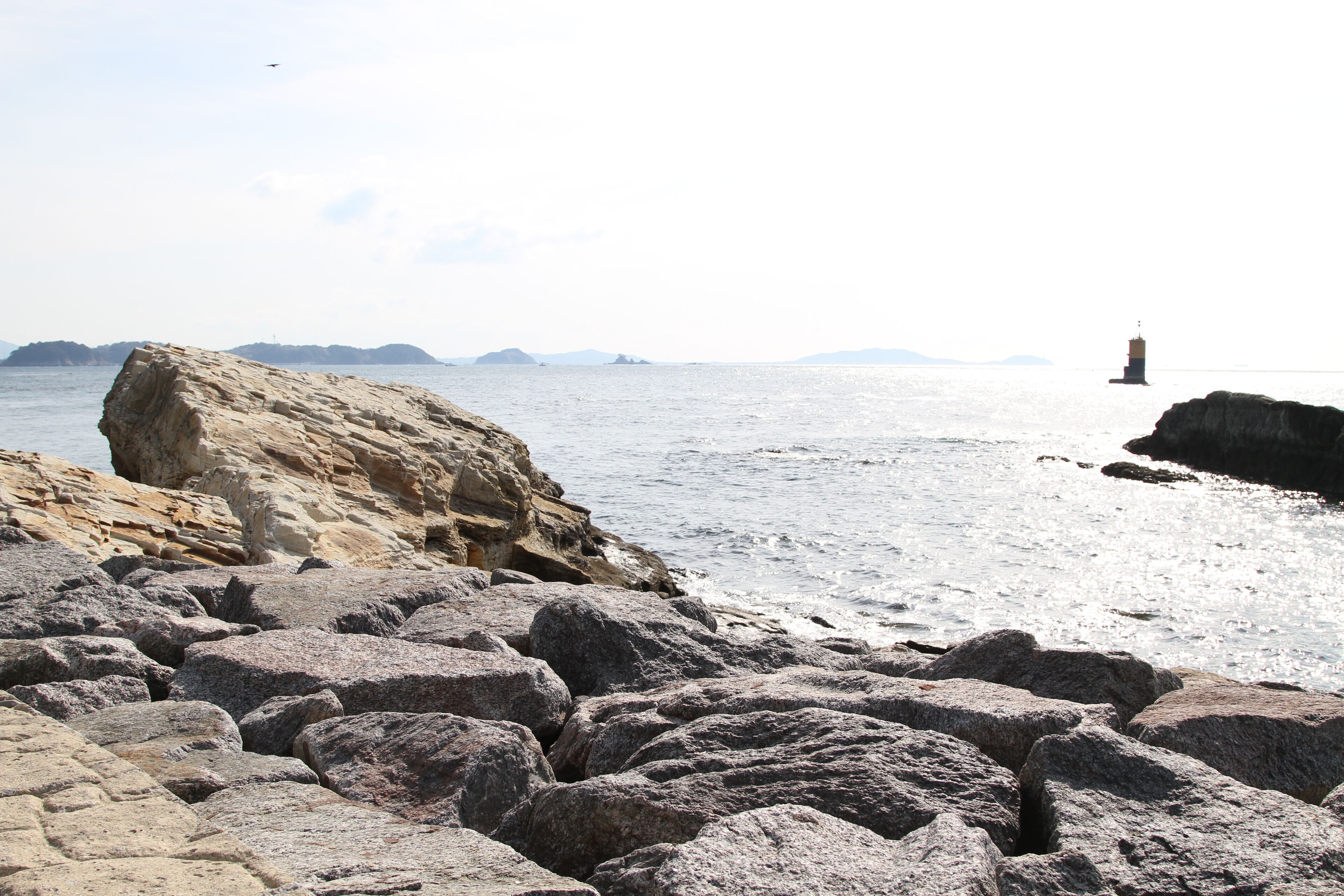 A rocky shoreline with large boulders and a distant lighthouse.