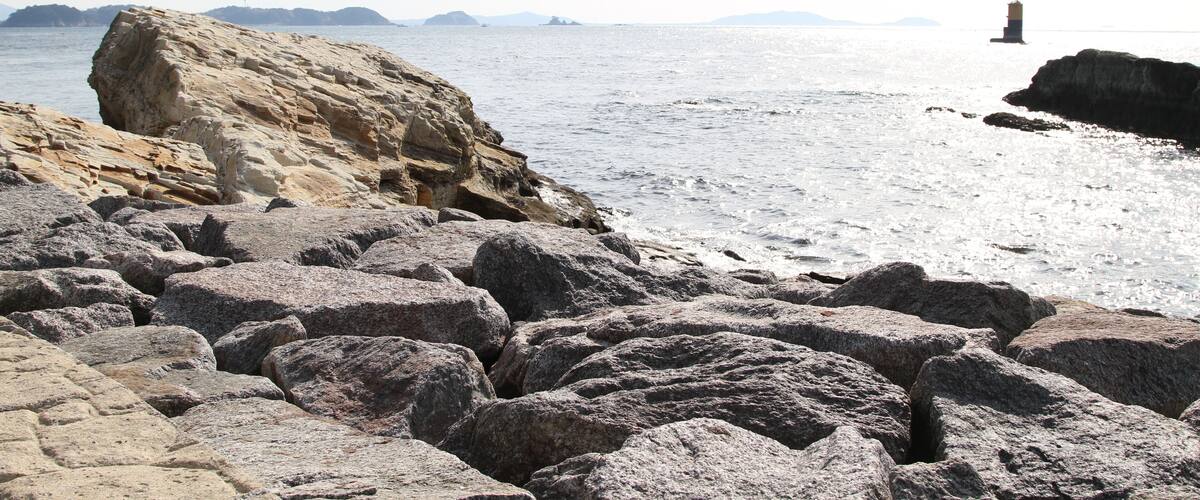 A rocky shoreline with large boulders and a distant lighthouse.