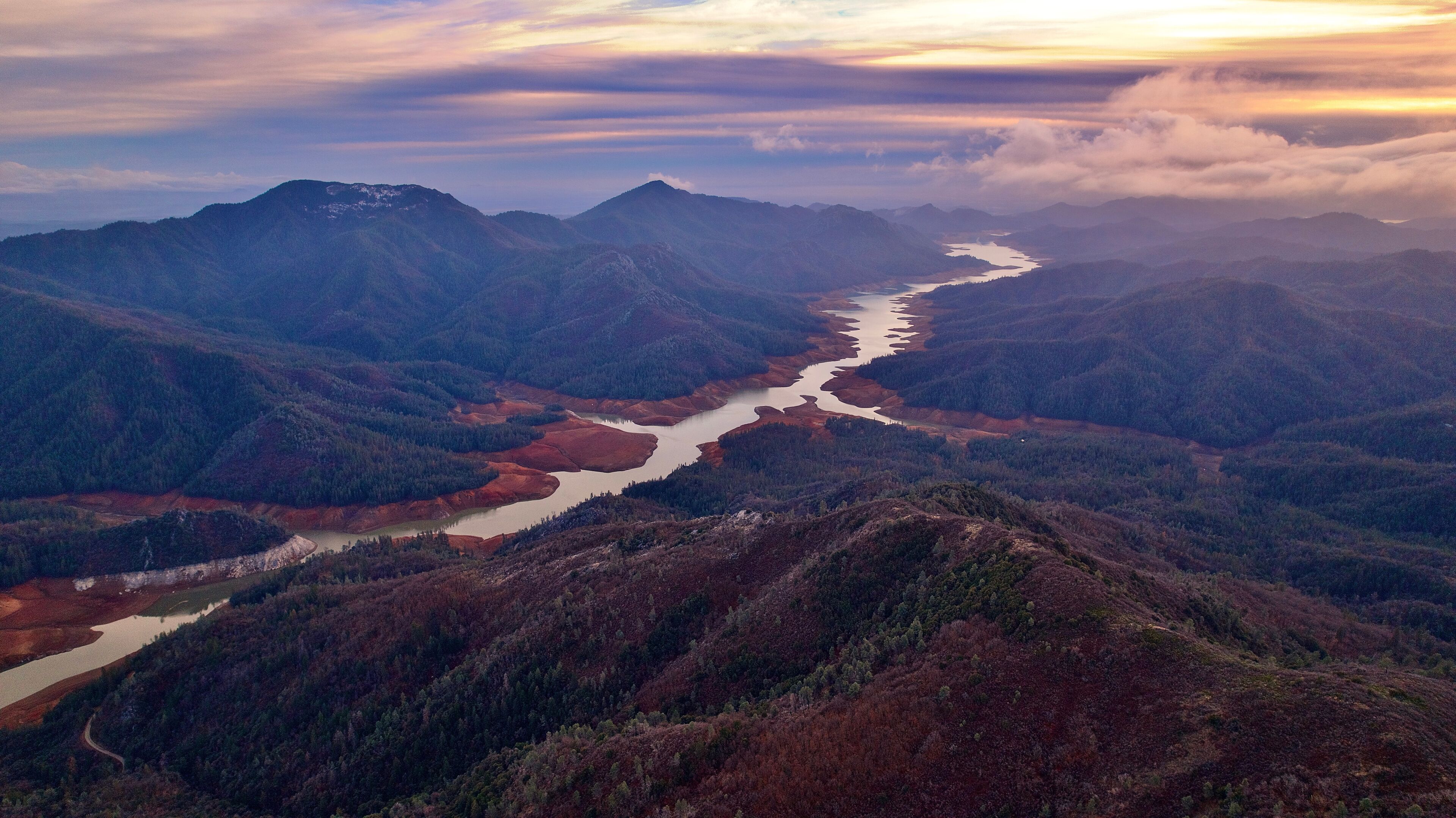A river winding through a mountainous landscape with dense forests and a clear sky.