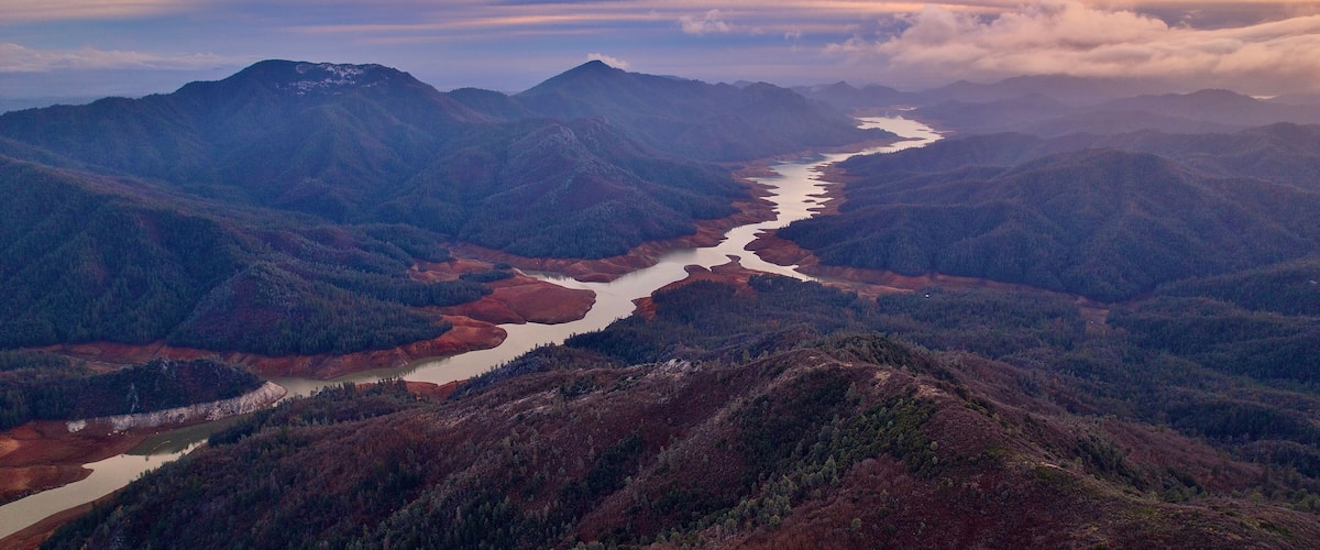 A river winding through a mountainous landscape with dense forests and a clear sky.